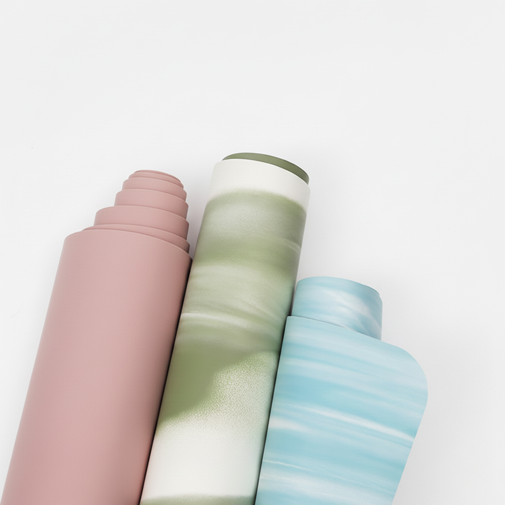 Three rolled-up workout yoga mats in various colors, including solid pink, green marble, and blue marble, standing upright against a plain background.