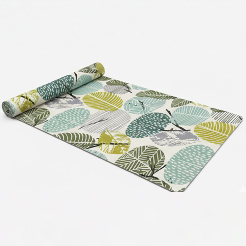 A nature-inspired custom suede yoga mat with a pattern of stylized leaves in various shades of green, grey, and beige, partially rolled to show the design.