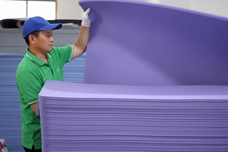 A factory worker inspects and stacks large sheets of purple yoga mat material during the production process.