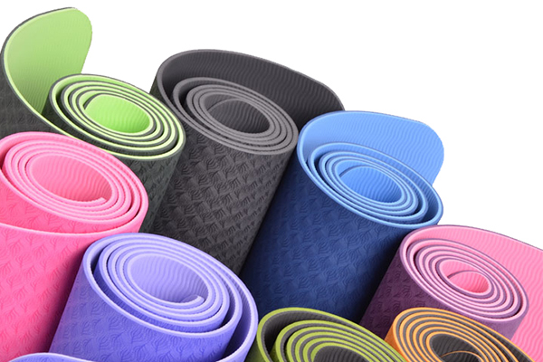 A vibrant collection of best-selling, lightweight TPE yoga mats in a variety of colors, rolled up to showcase their texture.