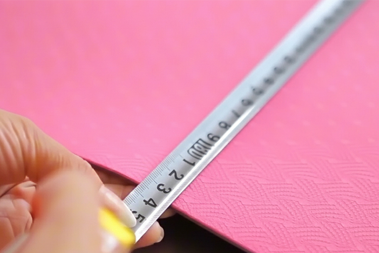 A quality control inspector is precisely measuring the thickness of a pink textured yoga mat to ensure it meets exact client specifications for a custom order.