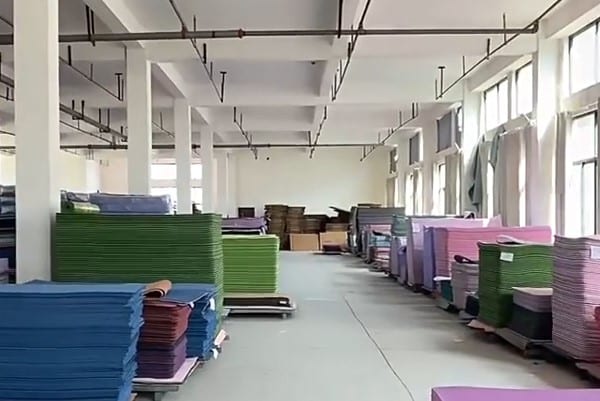 Interior of a large-scale yoga mat manufacturing facility showing organized stacks of colorful mats ready for custom OEM and bulk orders.